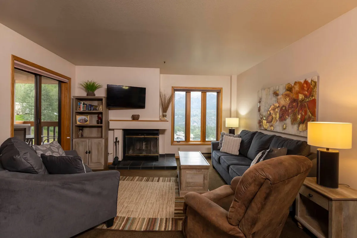This image showcases a warm and inviting living area centered around a crackling wood-burning fireplace. Plush sofas are arranged to encourage relaxation and conversation, while a large window offers a glimpse of the mountain view outside, bathing the space in natural light.