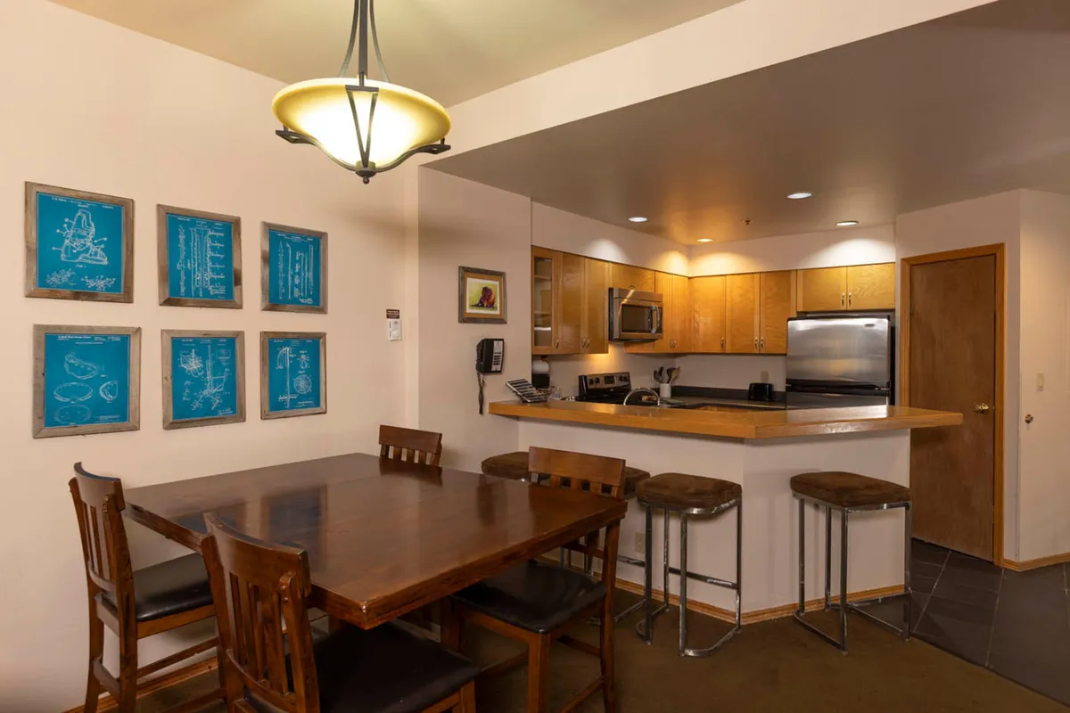 An open-plan dining and kitchen area, featuring a welcoming table for shared meals, bar stools at the counter, and vibrant artwork. Soft lighting enhances the inviting atmosphere, creating a perfect spot for couples to gather, share stories, or plan the next day’s adventures.
