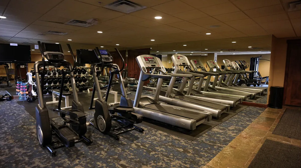A bright, modern fitness center equipped with elliptical machines, treadmills, free weights, and mirrored walls. The space looks energetic and inviting, perfect for guests who wish to maintain their workout routines during their stay.