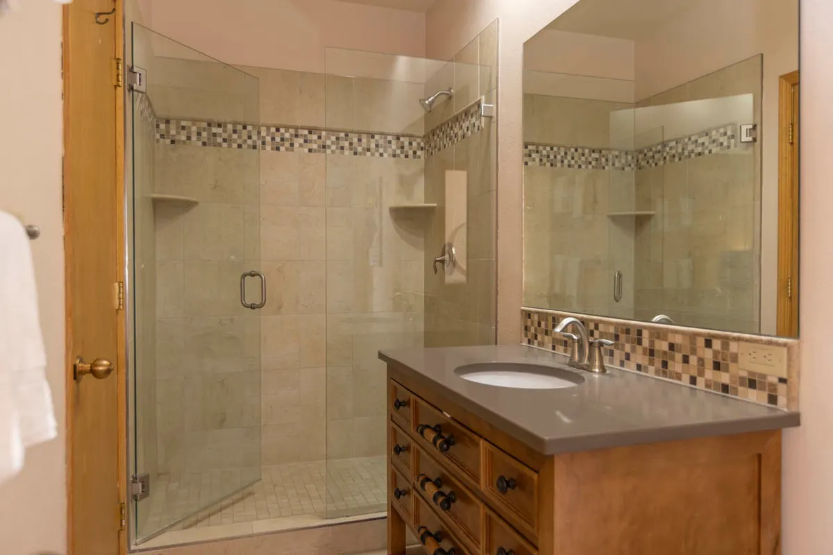 A modern, well-appointed bathroom with a glass shower enclosure, wooden vanity, and decorative tile accents. The clean lines and calming color palette create a soothing atmosphere ideal for unwinding after a busy day.