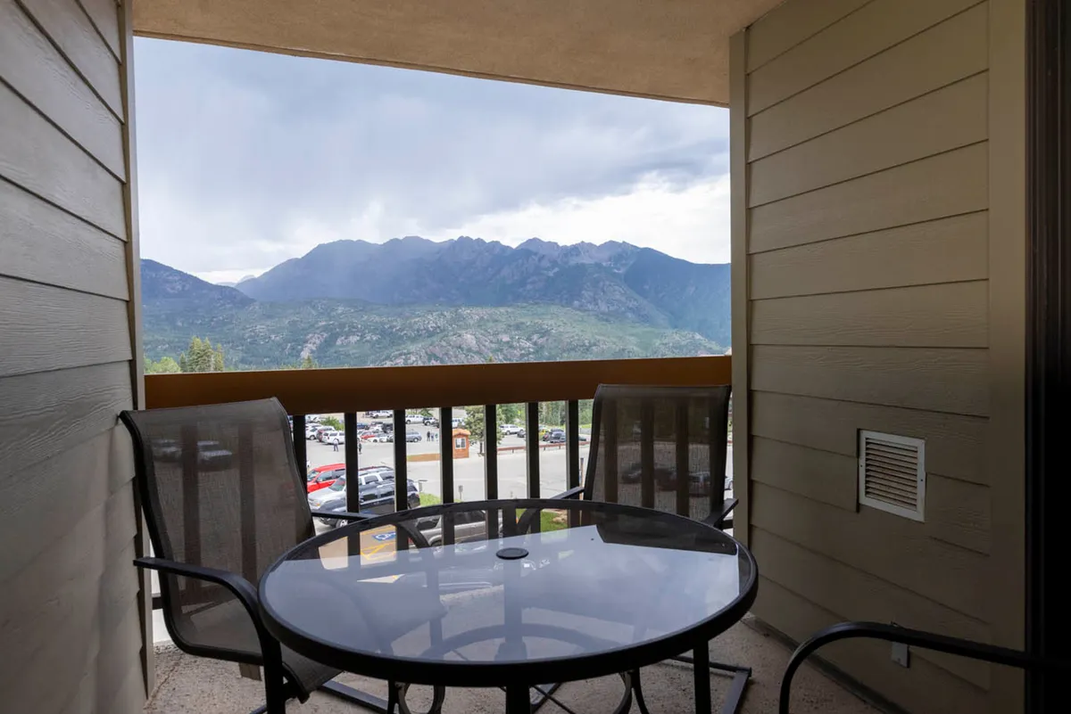 A scenic balcony with a table and chairs, offering an uninterrupted view of majestic mountains. The space is ideal for unwinding, whether enjoying morning coffee or admiring the sunset, and evokes the sensation of being elevated above the landscape.